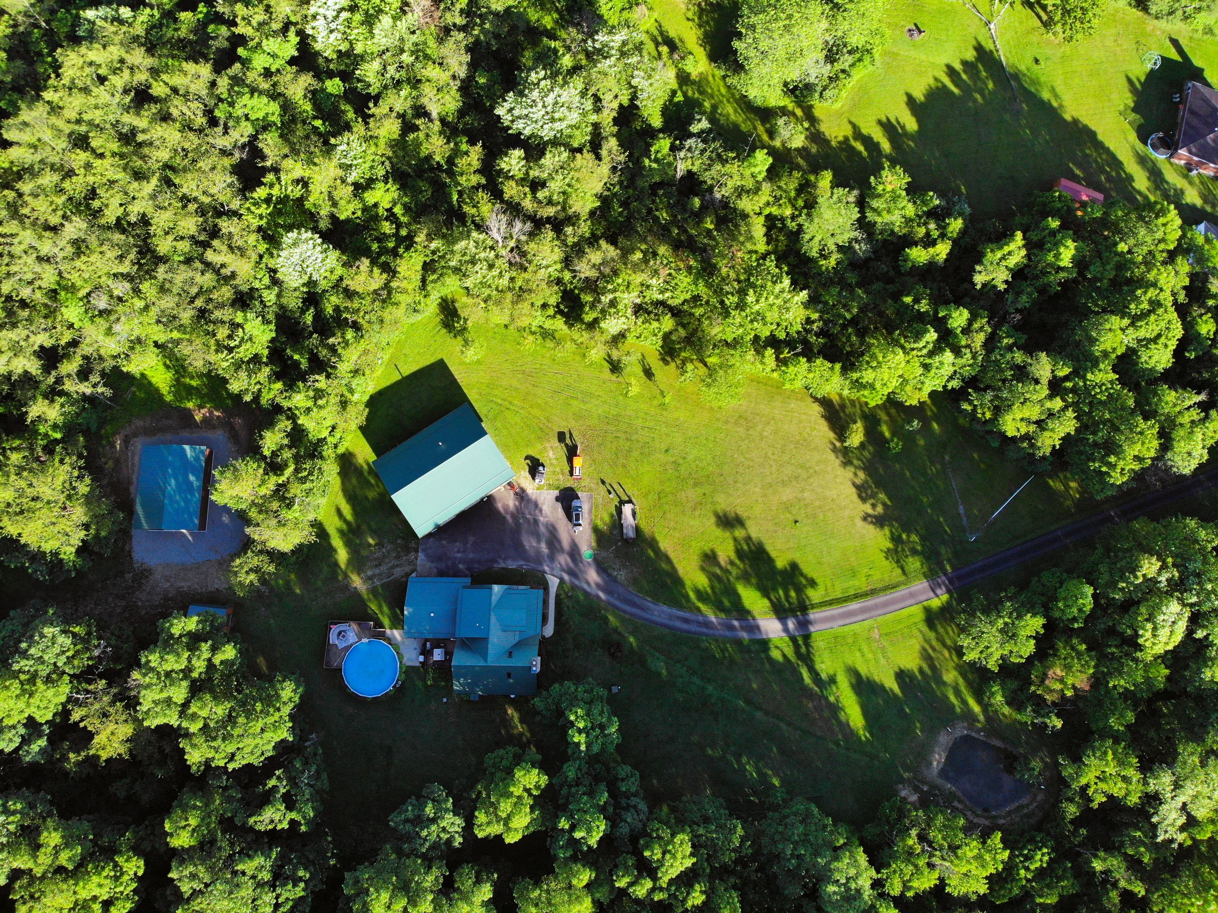 Aerial drone view of a rural home with metal-roof barn, pool, and driveway